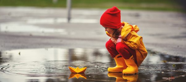 girl playing with paper boat on puddle