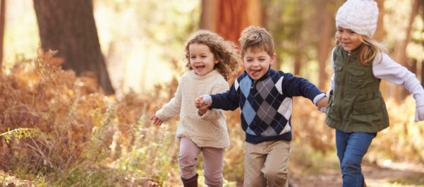 Three young happy children holding hands running through woods