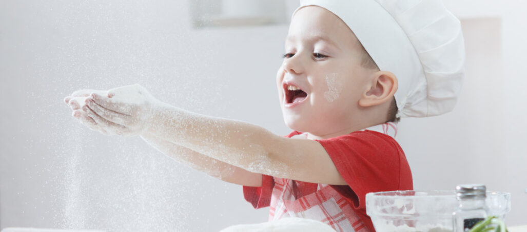 young boy in chef hat making pizza dough