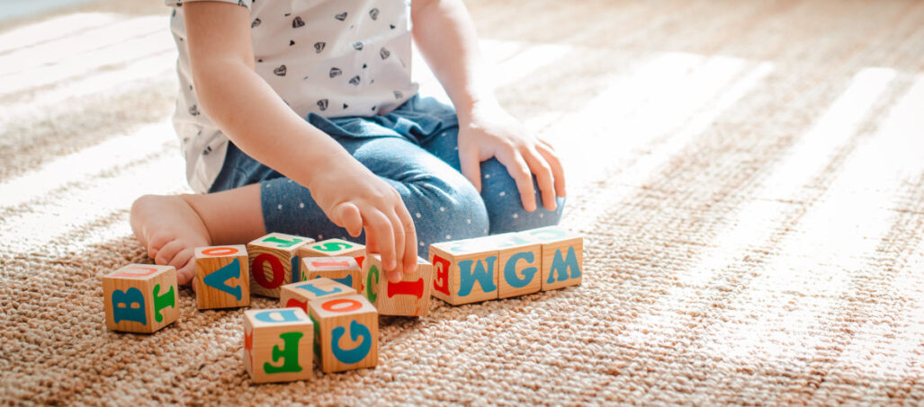 child plays with wooden blocks with letters on the floor