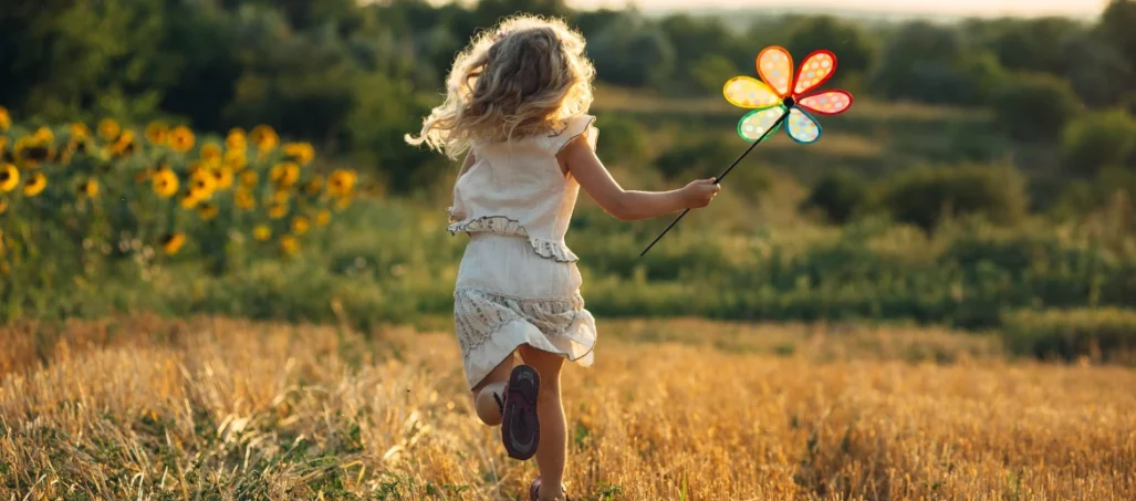 young girl running through wheatfield with toy windmill